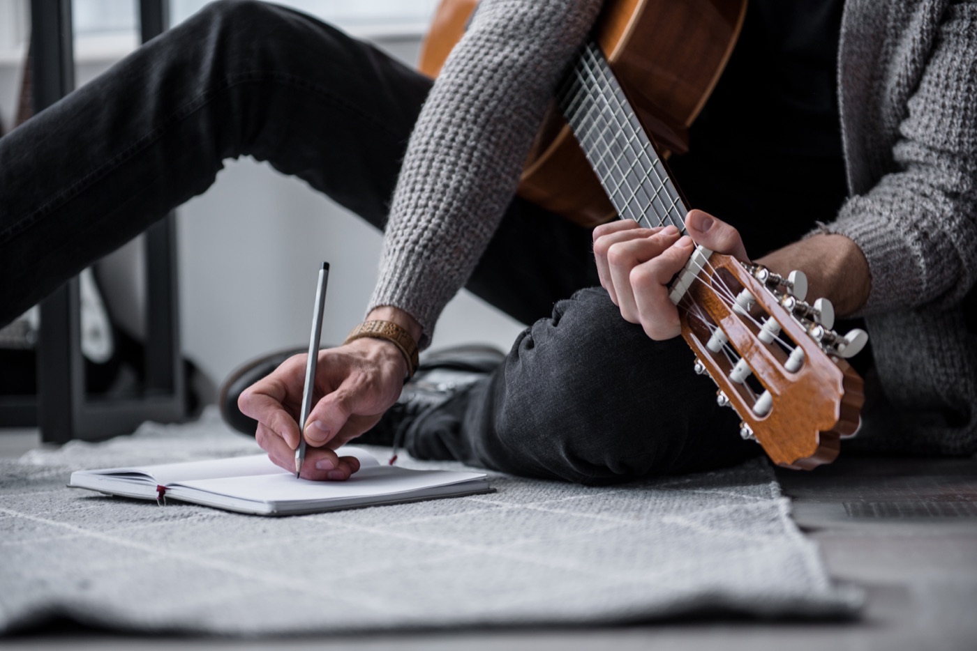 A songwriter writing in a notebook with a guitar in hand
